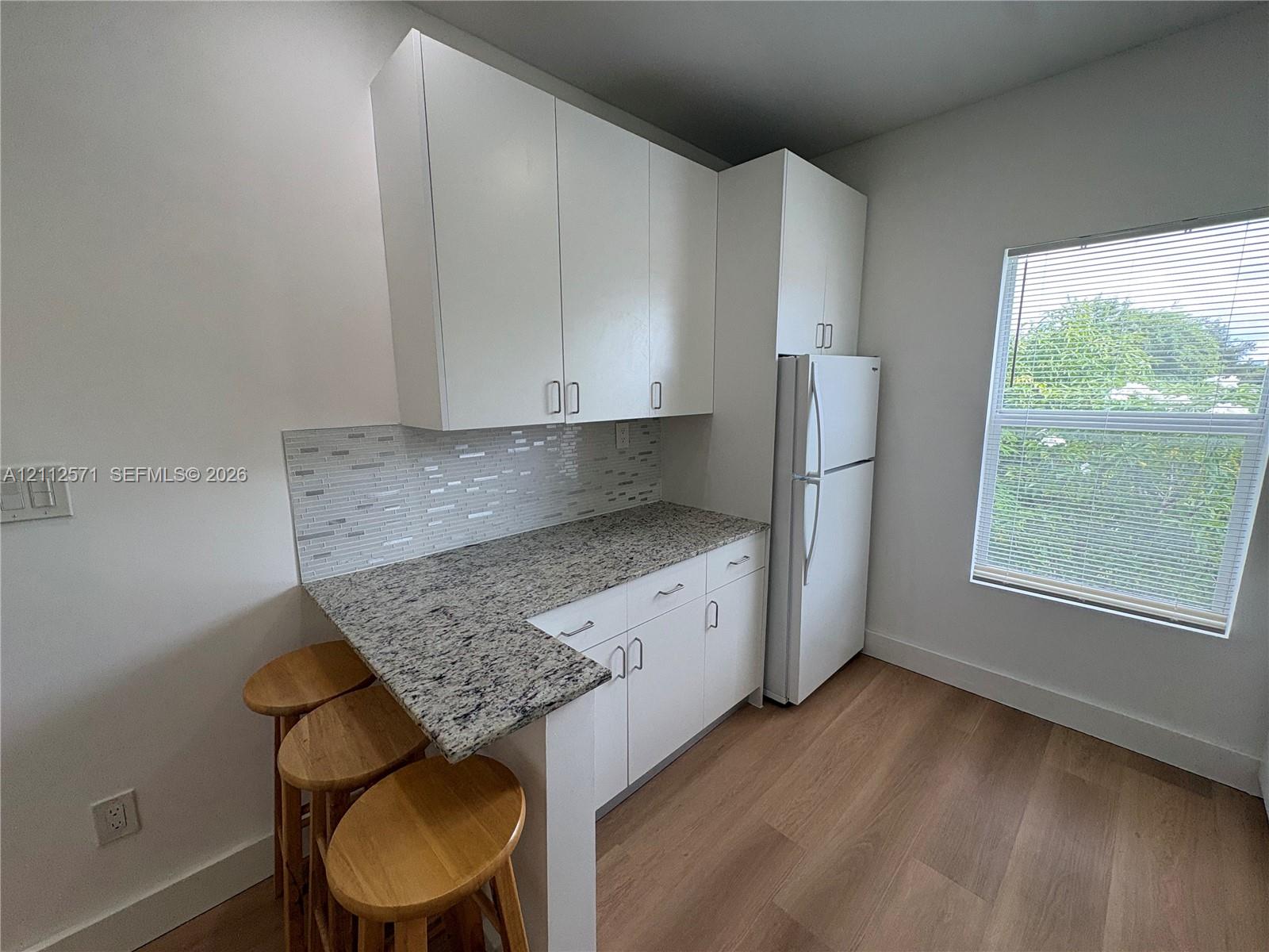White cabinetry, stone-finish countertop, linear tile backsplash, wood-finish flooring, and white appliance suite