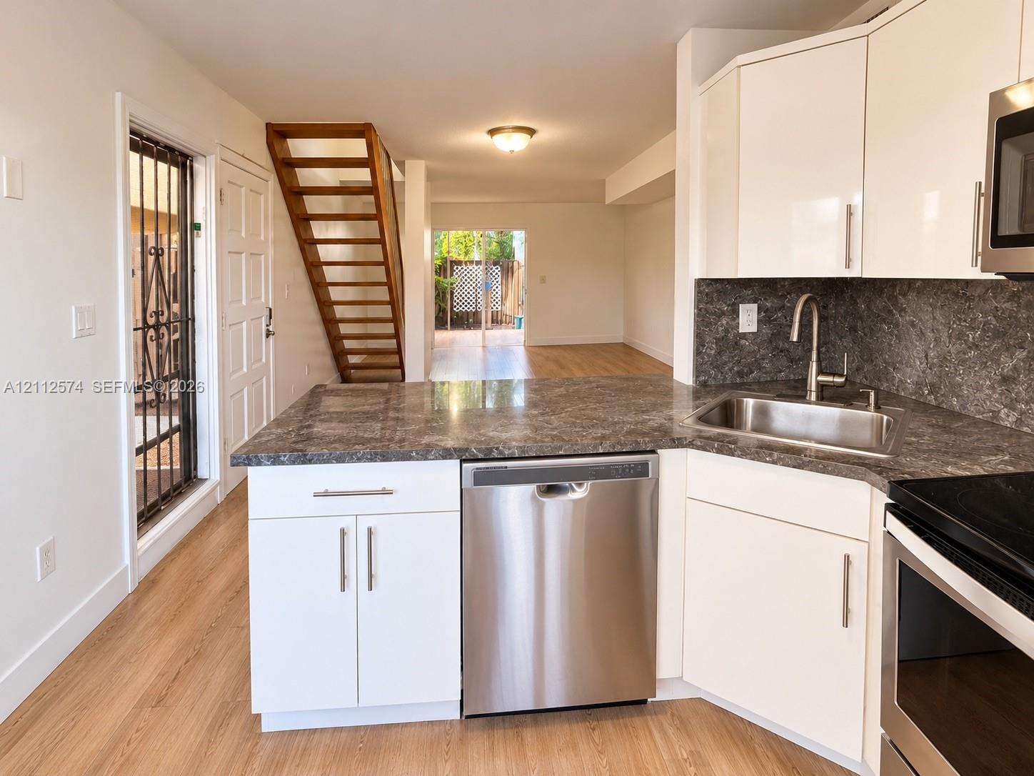 Kitchen featuring white cabinetry, stone-finish countertops, stainless steel appliances, wood-finish flooring, and an open-tread staircase