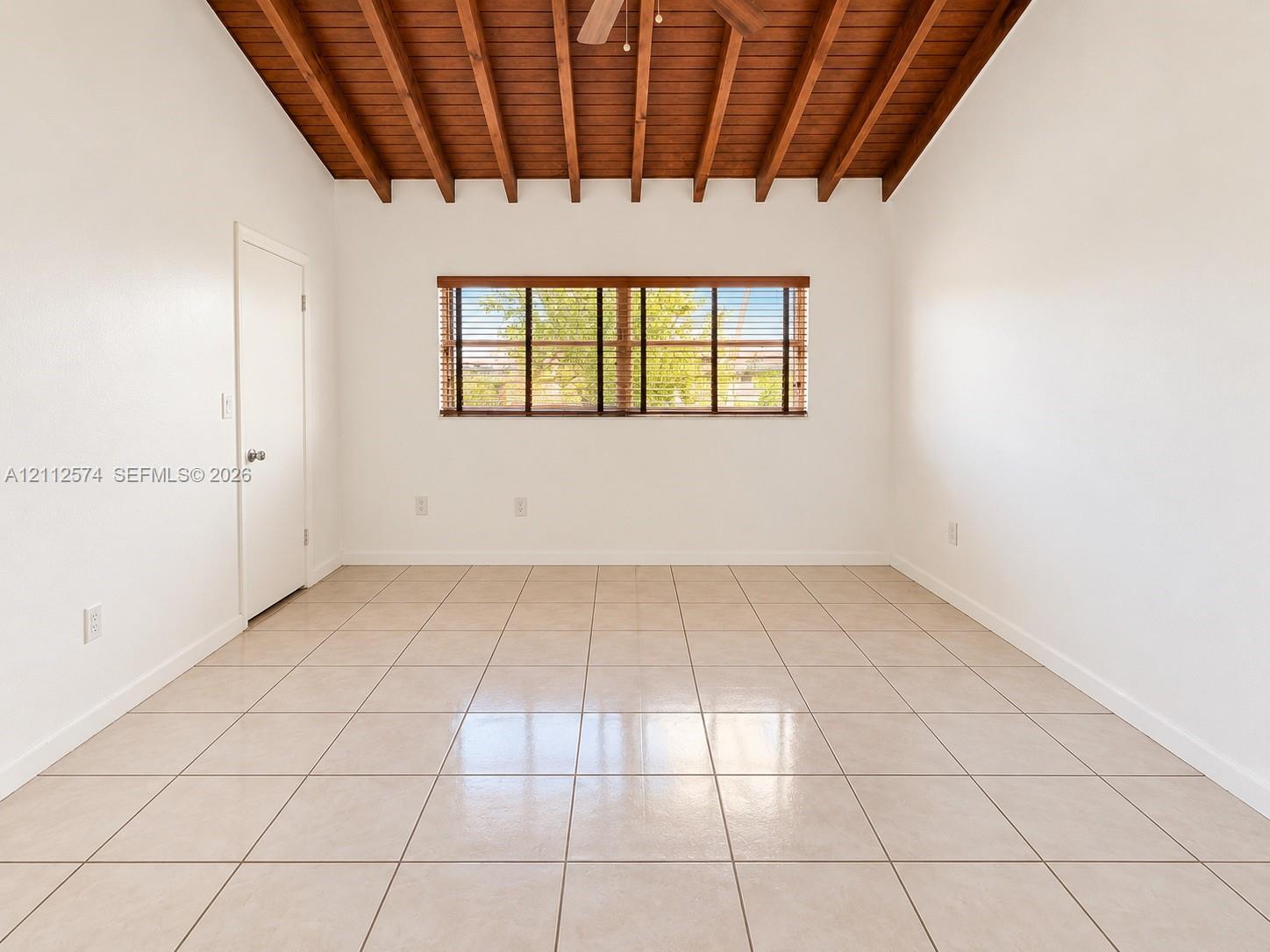 Exposed wood-beam vaulted ceiling featuring an integrated ceiling fan, large-format tile flooring, and horizontal window blinds