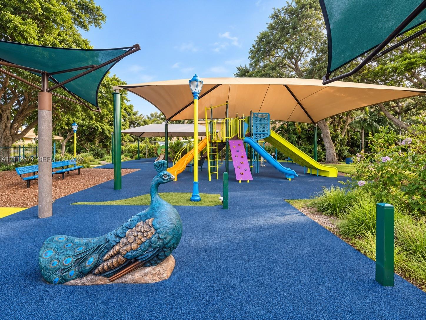 Recreational area featuring a playground structure with multiple slides, shade canopy, poured-in-place rubber surfacing, and decorative peacock sculpture
