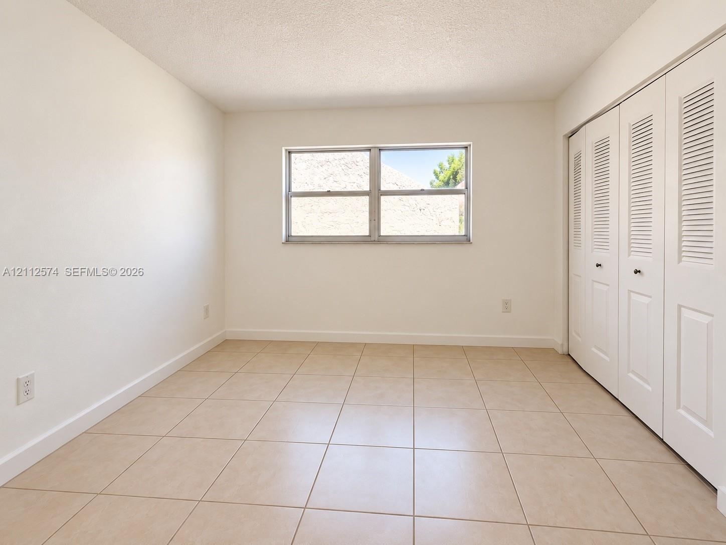Neutral tile flooring, sliding louvered closet doors, and a double-pane horizontal window