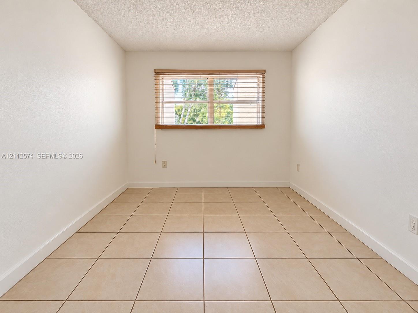 Neutral-toned tile flooring, textured ceiling, and a large central window with horizontal slat blinds