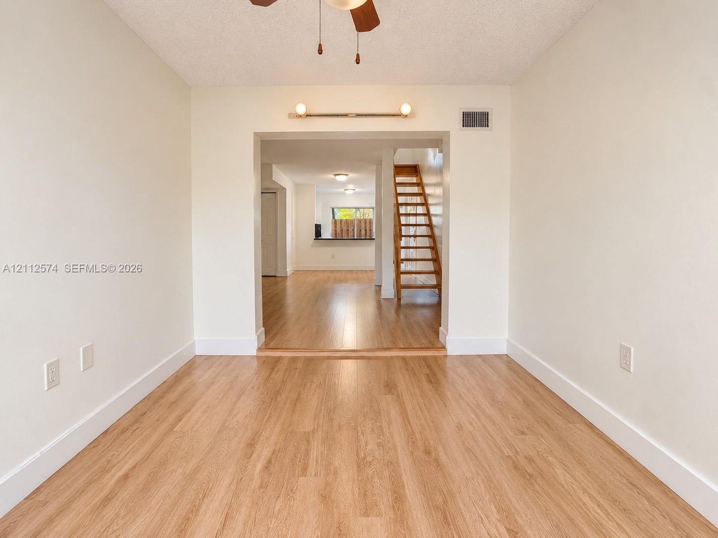 Wood-finish flooring, neutral wall tones, ceiling fan with integrated lighting, wall-mounted fixture, and wooden staircase