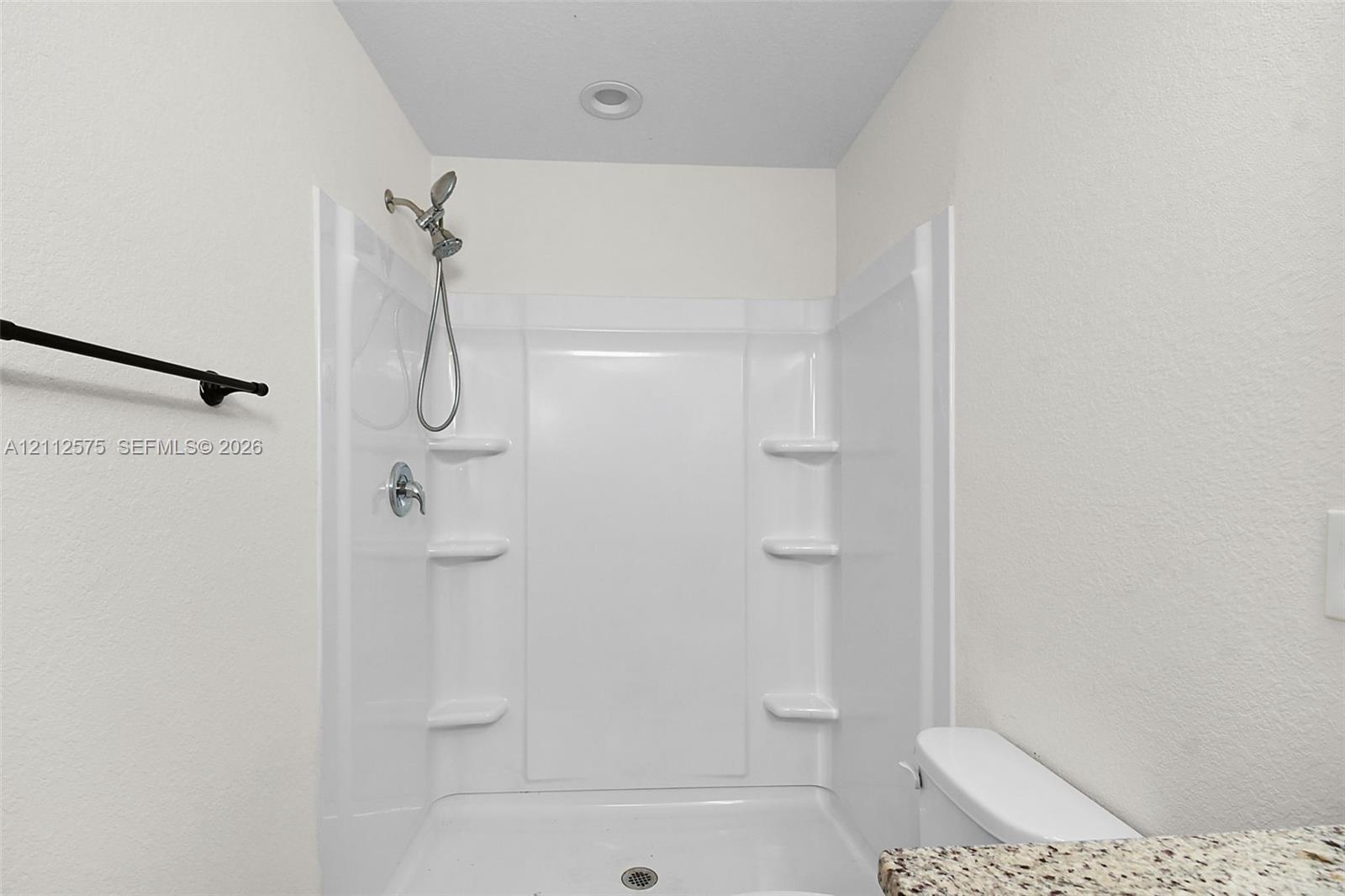 Walk-in shower enclosure with integrated shelving, handheld showerhead, recessed ceiling lighting, and a stone-finish countertop