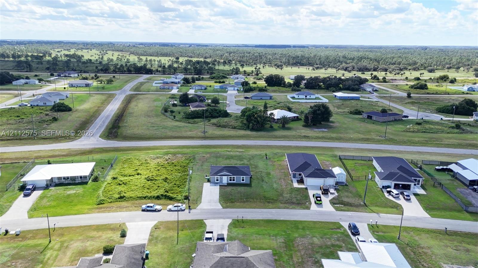 Aerial perspective of a residential street featuring paved roads, concrete driveways, and expansive undeveloped acreage