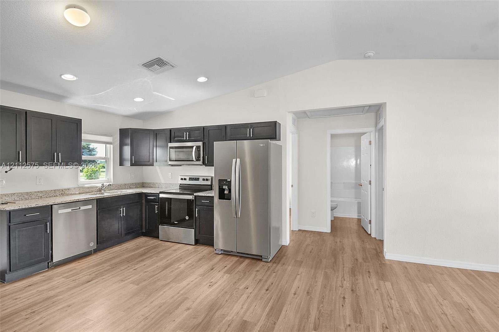 Kitchen featuring charcoal-toned cabinetry, light-toned stone-finish countertops, stainless steel appliances, recessed lighting, and wood-finish flooring