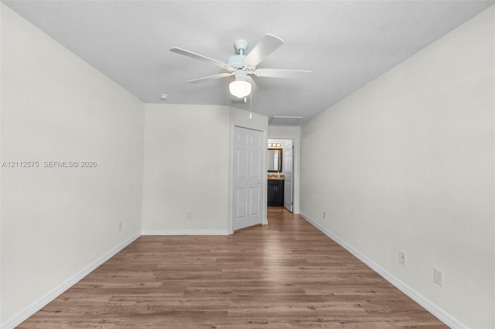 Interior space featuring wood-finish flooring, white walls, and a ceiling fan with integrated lighting