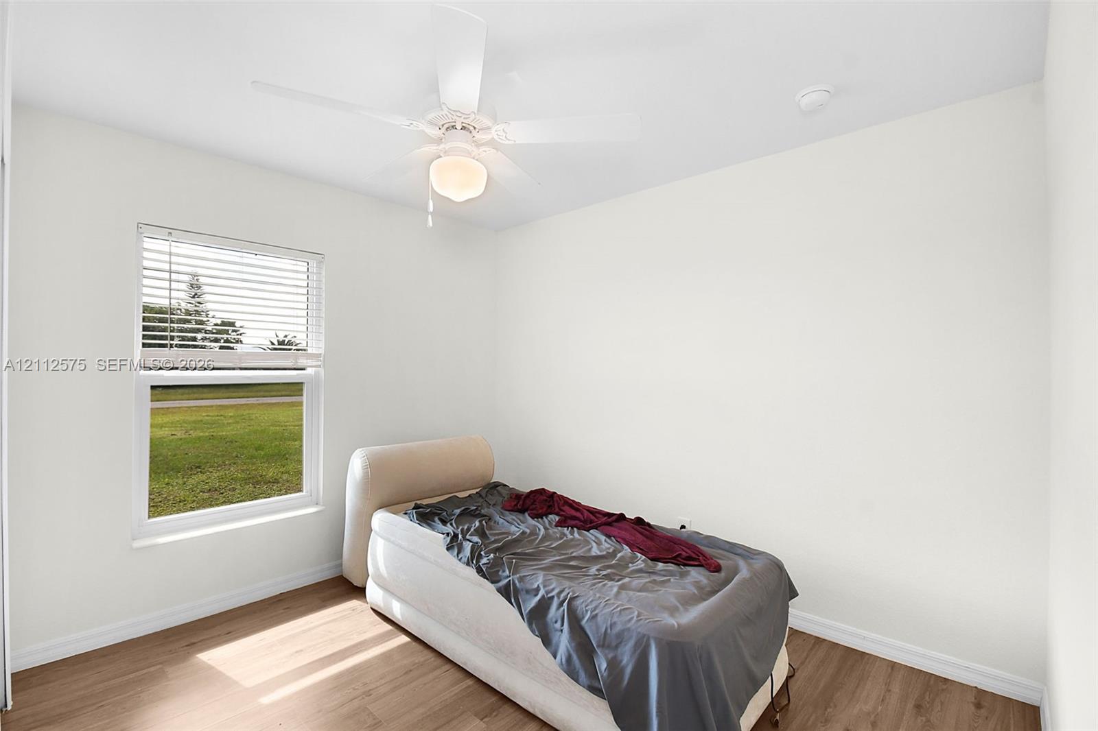 Room featuring wood-finish flooring, a white ceiling fan with integrated lighting, and a single-pane window with horizontal blinds