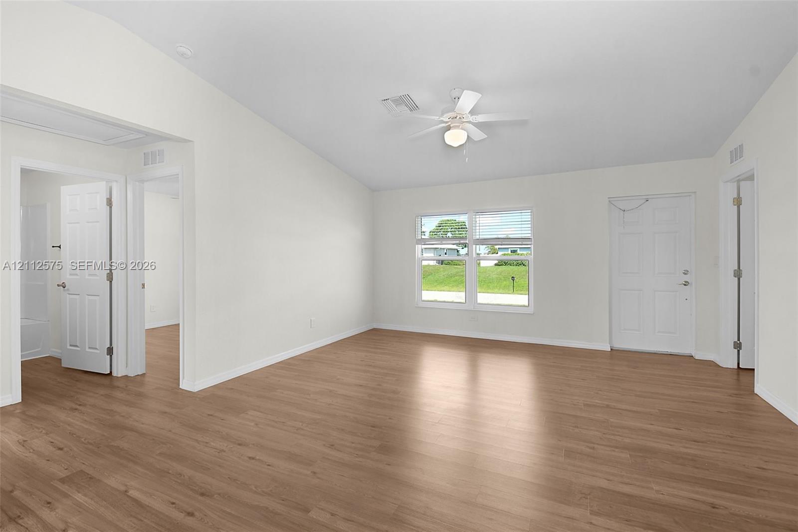 Interior space featuring wood-finish flooring, vaulted ceilings, a central ceiling fan with integrated lighting, dual-pane windows, and multi-panel interior doors
