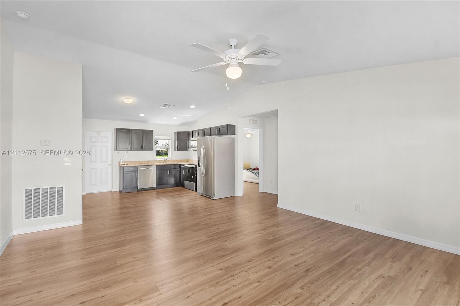 Open-concept area featuring vaulted ceilings, wood-finish flooring, ceiling fan, and cabinetry with stainless steel appliances