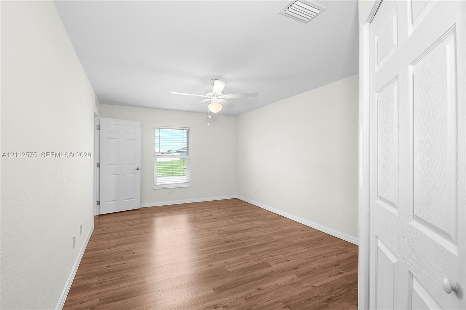Room featuring wood-finish flooring, a white ceiling fan with integrated light, a single-hung window, and white six-panel interior doors