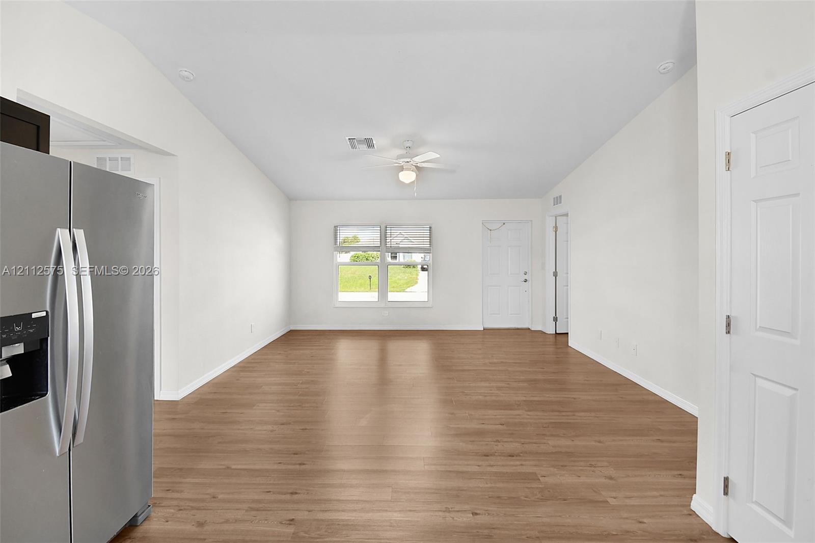 Open interior space featuring wood-finish flooring, vaulted ceilings, a ceiling fan with light fixture, and large windows providing natural illumination