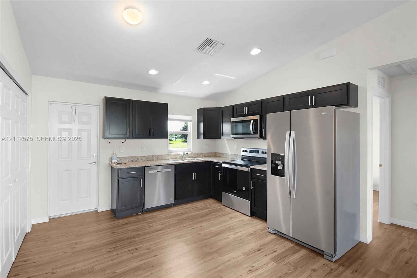 Kitchen featuring dark cabinetry, stone-surface countertops, wood-finish flooring, and stainless steel appliances including a side-by-side refrigerator, microwave, and dishwasher