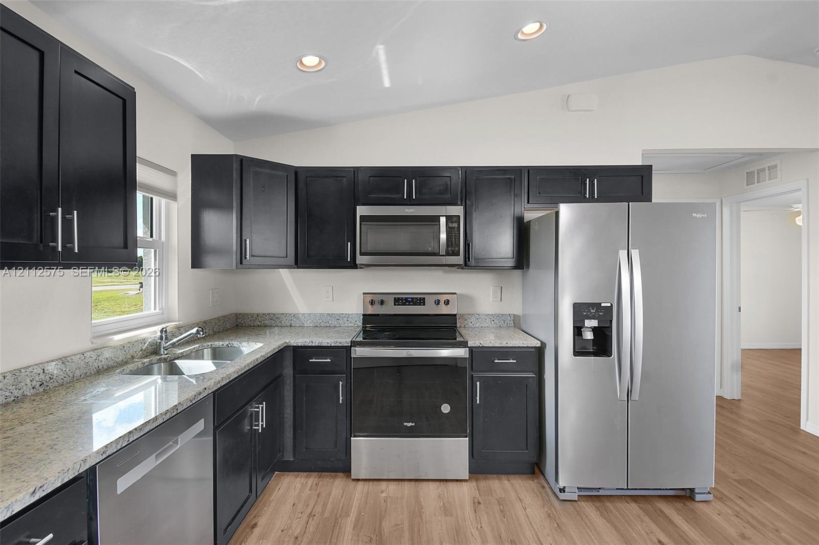 Kitchen featuring dark cabinetry, stone-finish countertops, stainless steel appliances, and wood-finish flooring