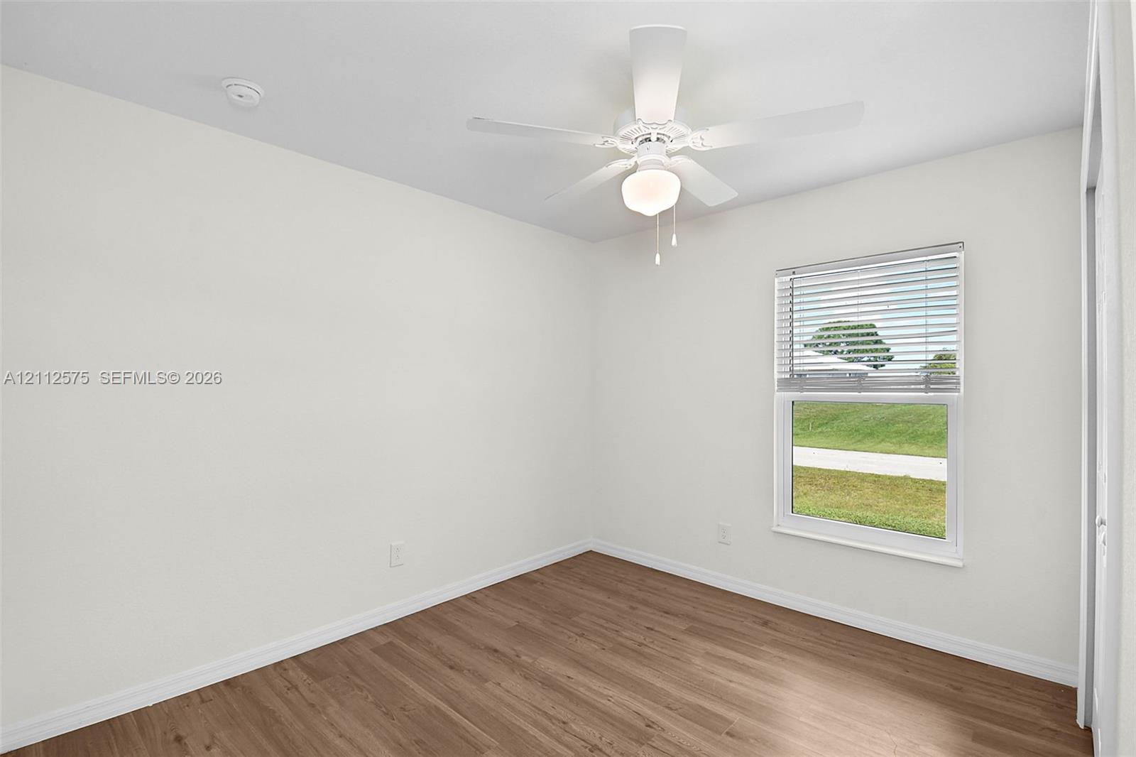 Interior room featuring wood-finish flooring, white walls, a ceiling fan with integrated lighting, and a single-hung window with blinds