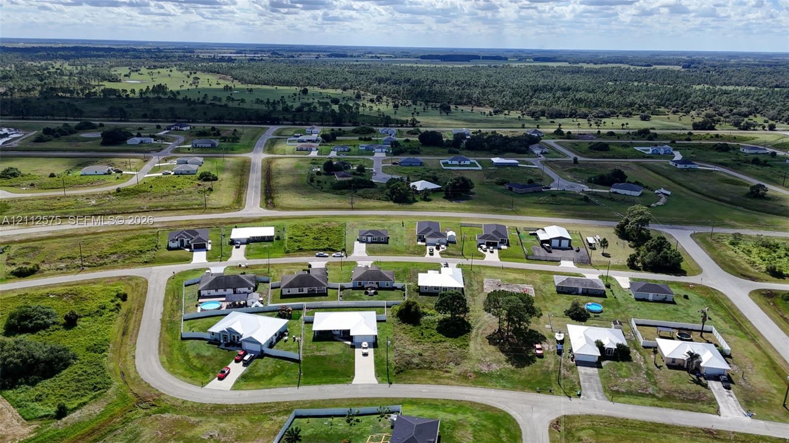 Aerial perspective of a suburban neighborhood featuring paved streets, grass-covered lots, and residential structures with metal roofing