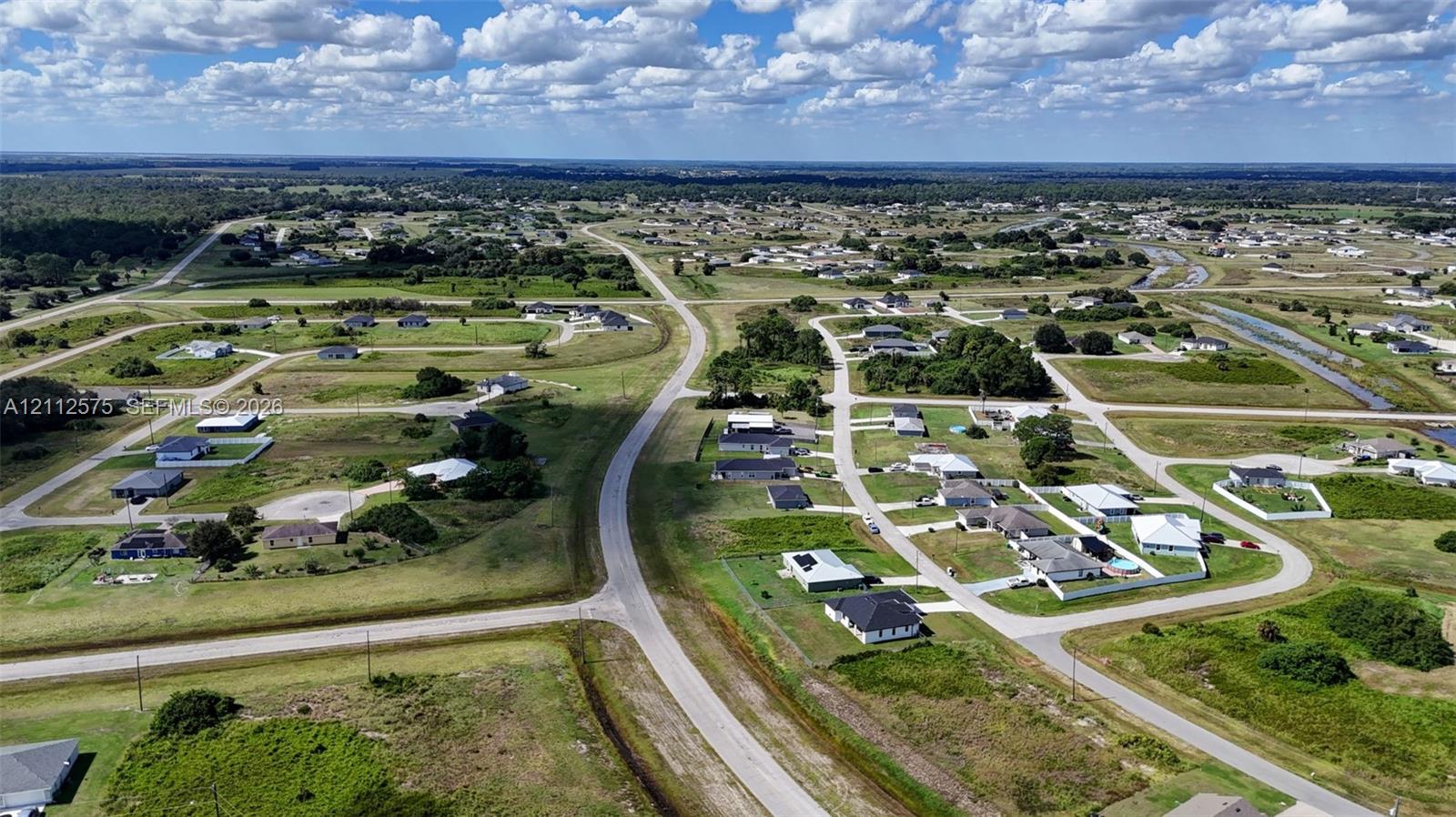 Aerial perspective of residential area featuring paved streets, grass-covered lots, and residential structures with dark-toned roofing