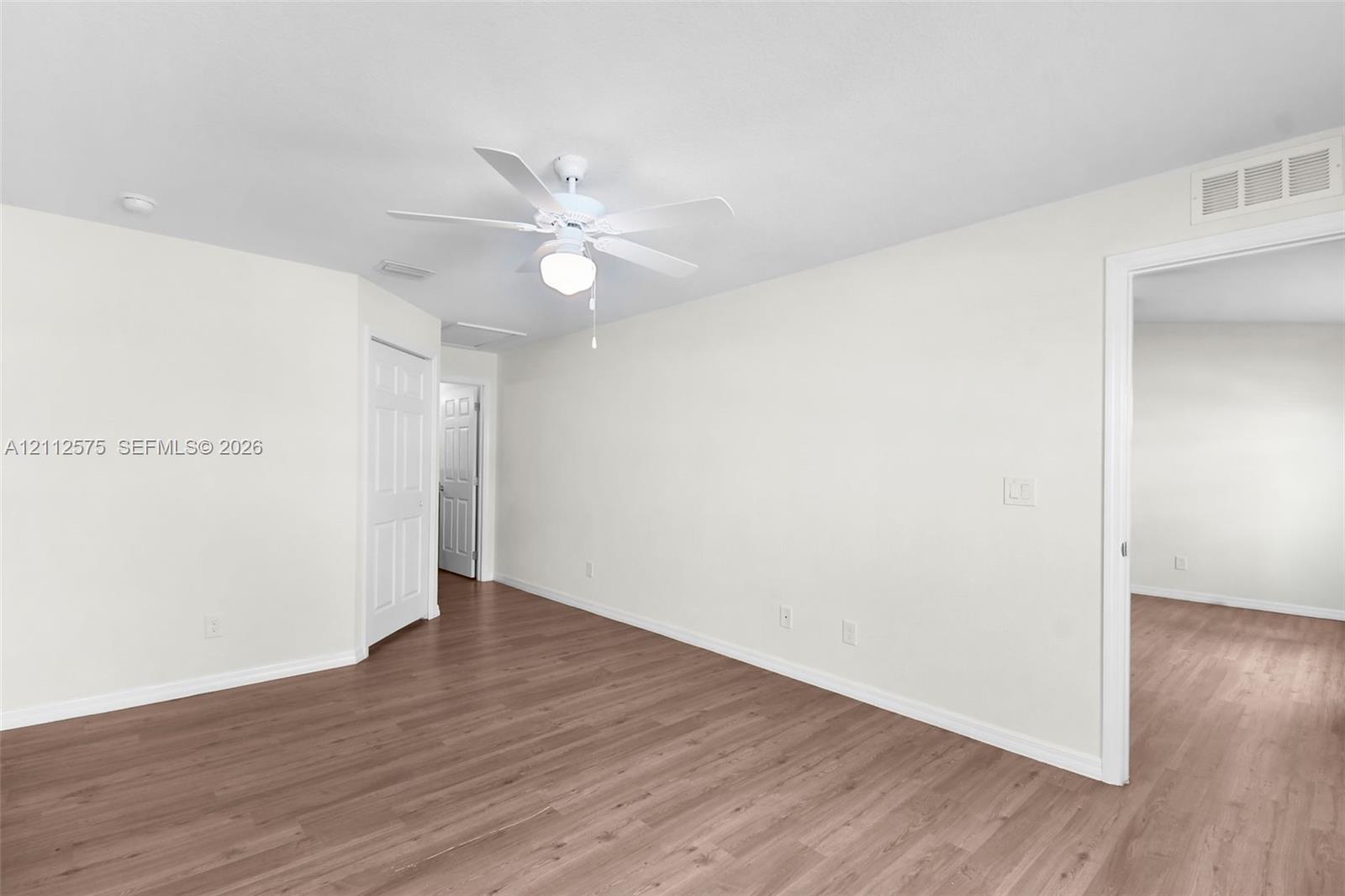 Neutral-toned interior space featuring wood-finish flooring, a ceiling-mounted light fixture, and panel-style interior doors