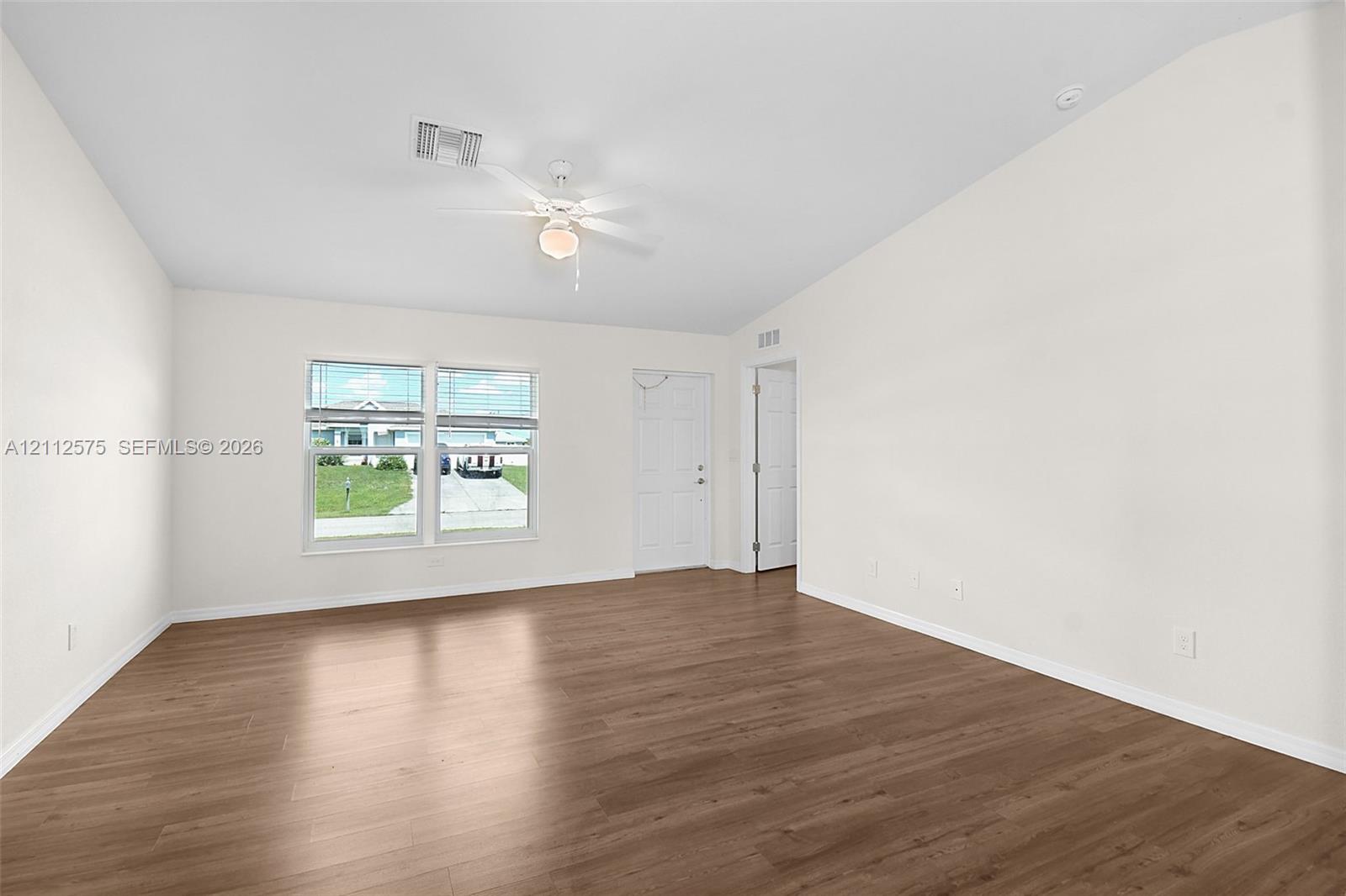 Neutral-toned interior featuring wood-finish flooring, vaulted ceilings, multi-pane windows, and an attached ceiling fan with integrated lighting