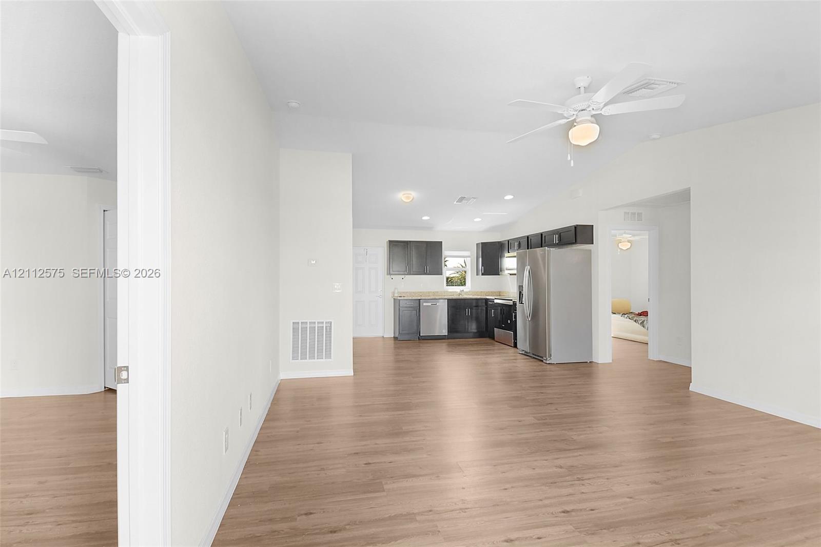 Open-concept interior featuring light wood-finish flooring, vaulted ceilings with a mounted paddle fan, and a kitchen equipped with dark-toned cabinetry, light-colored countertops, and stainless steel appliances