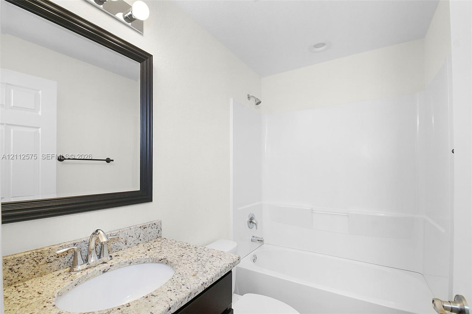 Bathroom featuring a stone-look countertop, undermount sink, dark-framed mirror, and a combination tub and shower surround