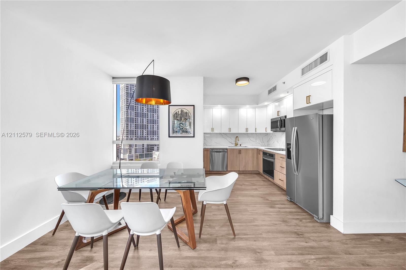 Kitchen featuring wood-finish cabinetry, white upper cabinets, stone-look backsplash, stainless steel appliances, and wood-finish flooring Kitchen featuring wood-finish cabinetry, white upper cabinets, stone-look backsplash, stainless steel appliances, and wood-finish flooring