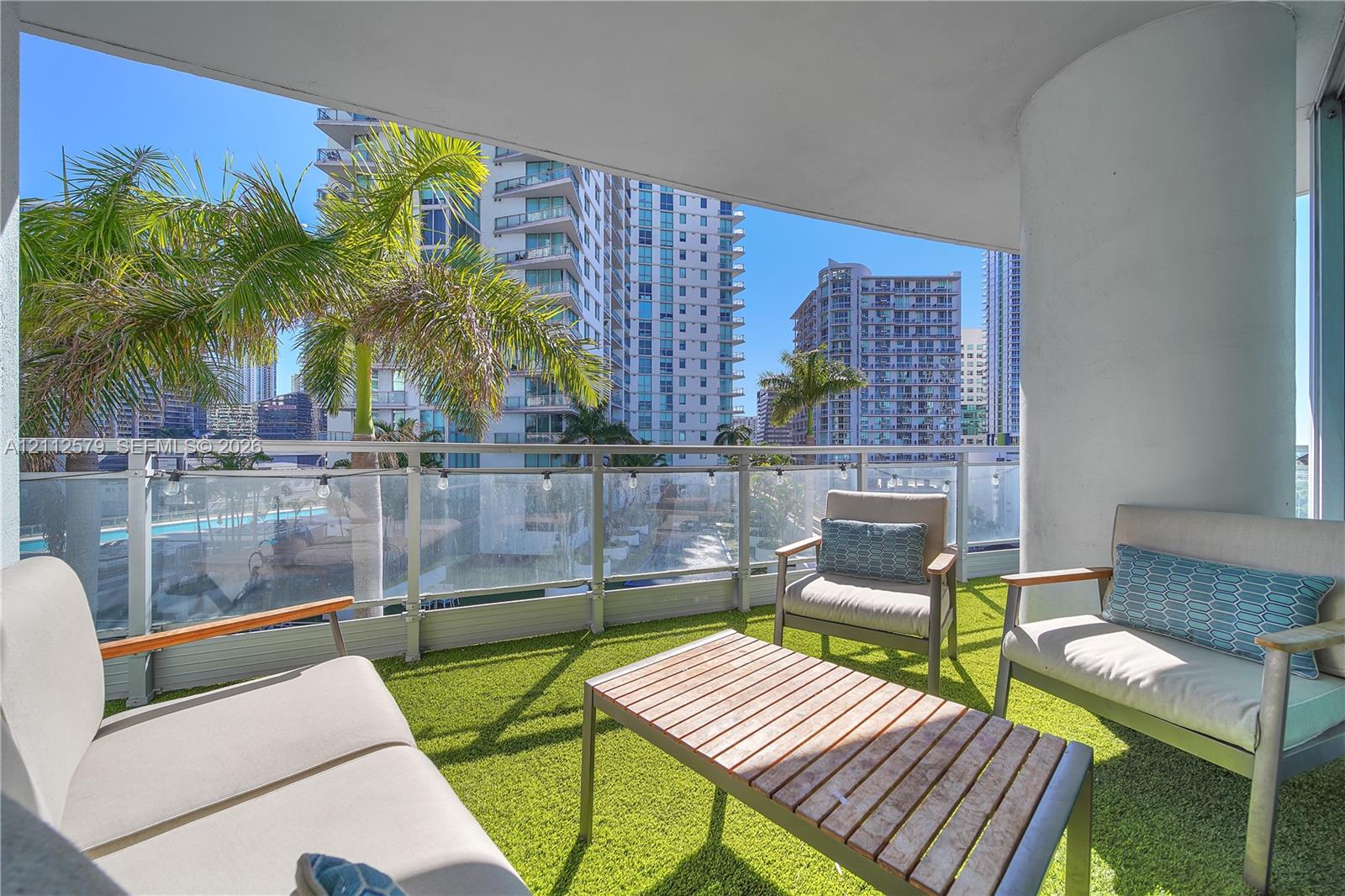 Covered balcony featuring artificial turf flooring, a metal and glass railing system, and a structural concrete column Covered balcony featuring artificial turf flooring, a metal and glass railing system, and a structural concrete column