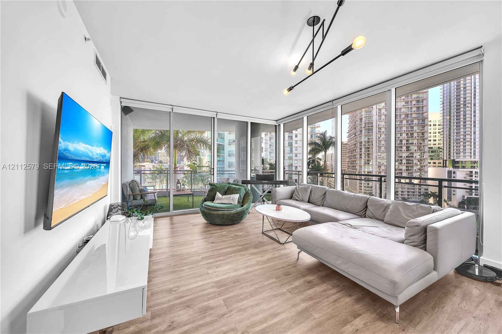 Floor-to-ceiling windows, wood-finish flooring, linear multi-arm light fixture, and an attached balcony with metal railing Floor-to-ceiling windows, wood-finish flooring, linear multi-arm light fixture, and an attached balcony with metal railing