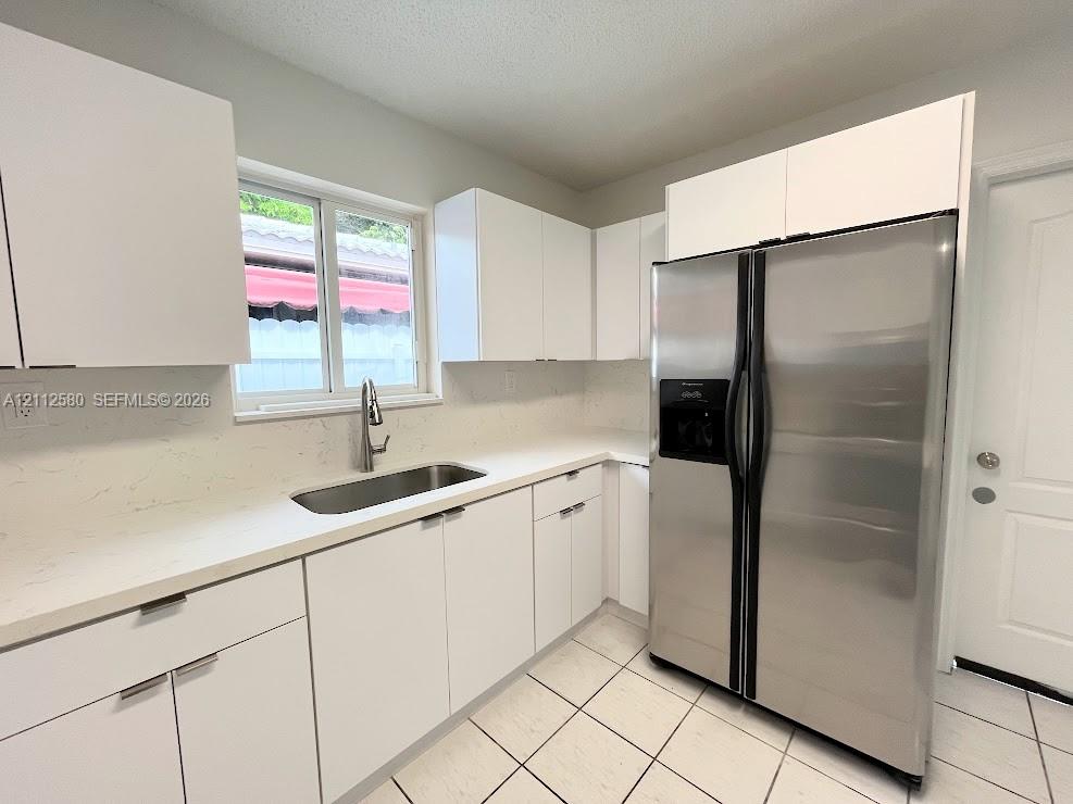 Kitchen featuring white flat-panel cabinetry, light-colored quartz countertops, stainless steel side-by-side refrigerator, under-mount sink with pull-down faucet, and tile flooring Kitchen featuring white flat-panel cabinetry, light-colored quartz countertops, stainless steel side-by-side refrigerator, under-mount sink with pull-down faucet, and tile flooring