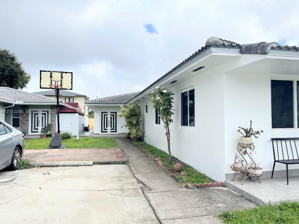 Exterior facade featuring a concrete tile roof, crisp white stucco finish, dual-entry doors with geometric detailing, and paved driveway space