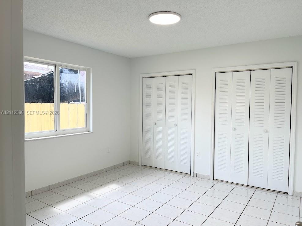 Interior room featuring white tile flooring, two sets of white louvered-panel closet doors, and a large horizontal window