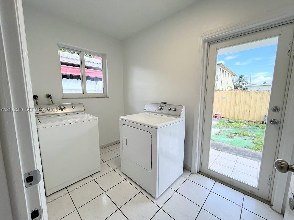 Laundry room featuring large-format ceramic tile flooring, a window, and a glass-paneled exterior door Laundry room featuring large-format ceramic tile flooring, a window, and a glass-paneled exterior door