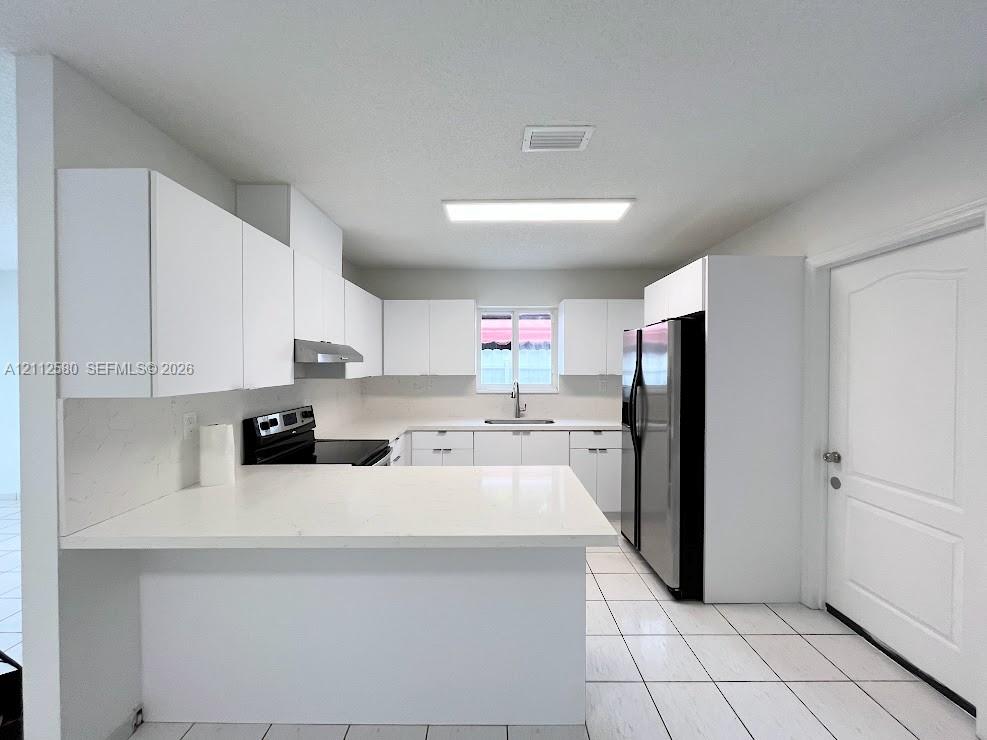 Kitchen featuring flat-panel white cabinetry, quartz countertops, tile flooring, and integrated black appliances Kitchen featuring flat-panel white cabinetry, quartz countertops, tile flooring, and integrated black appliances