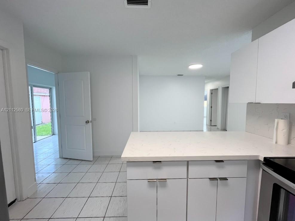 Kitchen featuring white cabinetry, light-toned stone-finish countertops, tile flooring, and integrated stainless steel appliances Kitchen featuring white cabinetry, light-toned stone-finish countertops, tile flooring, and integrated stainless steel appliances