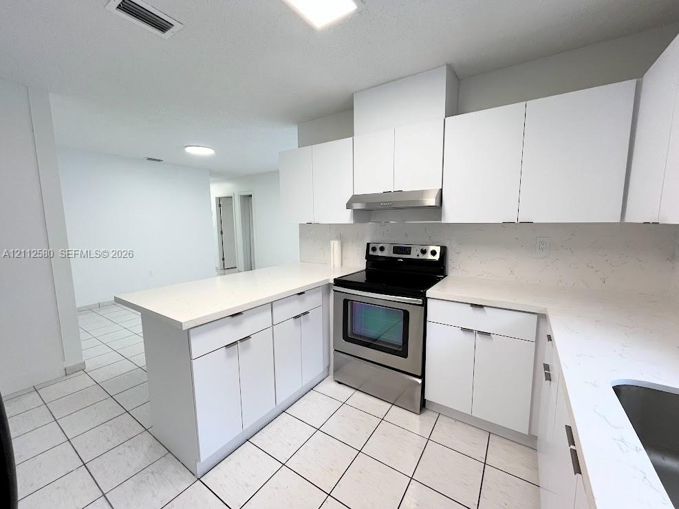 Kitchen featuring flat-panel white cabinetry, stone-finish countertops, stainless steel range with overhead hood, and tile flooring Kitchen featuring flat-panel white cabinetry, stone-finish countertops, stainless steel range with overhead hood, and tile flooring