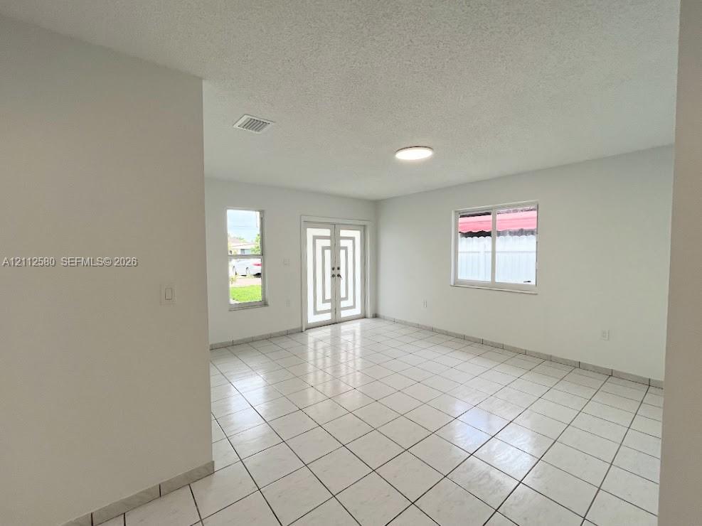 Interior space featuring white tile flooring, neutral walls, double front doors with geometric glass detailing, and dual-pane windows Interior space featuring white tile flooring, neutral walls, double front doors with geometric glass detailing, and dual-pane windows