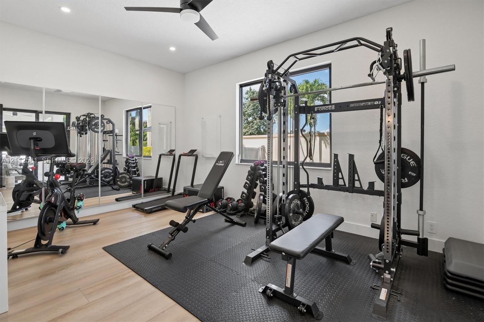 Room featuring wood-finish flooring, recessed lighting, a ceiling fan, a floor-to-ceiling mirror wall, and a large window