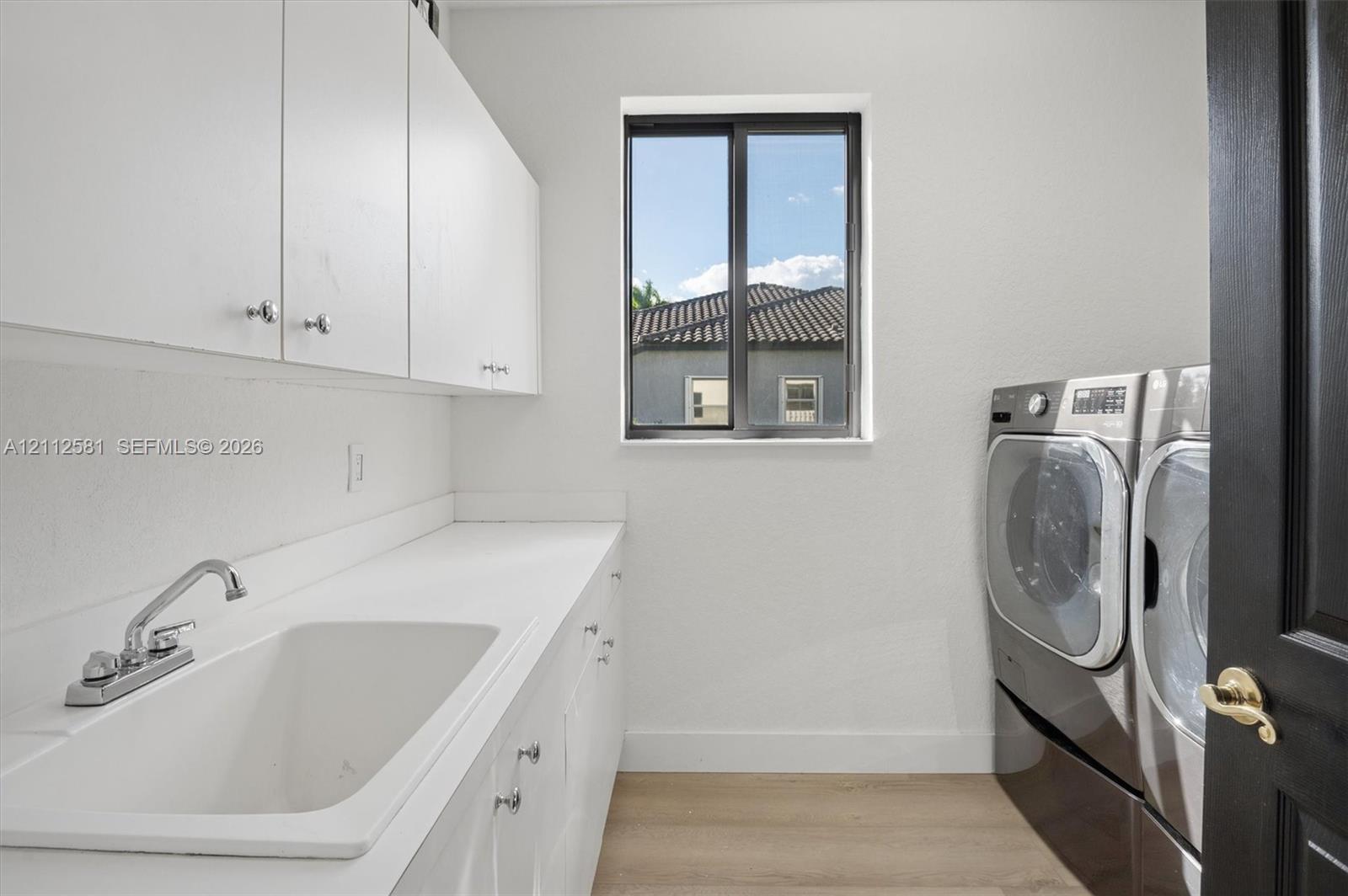 Laundry space featuring custom white cabinetry, a built-in utility sink with a chrome faucet, solid-surface countertops, and wood-finish flooring