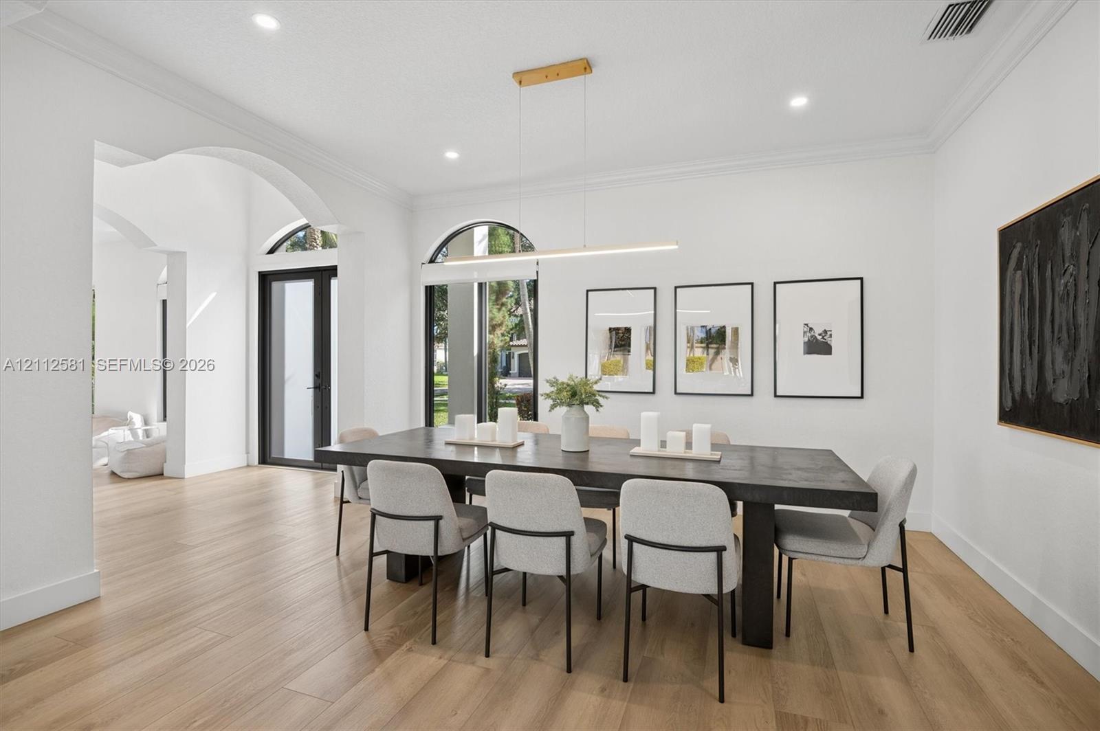 Dining space featuring wood-finish flooring, arched windows, crown molding, recessed lighting, and a modern linear pendant fixture