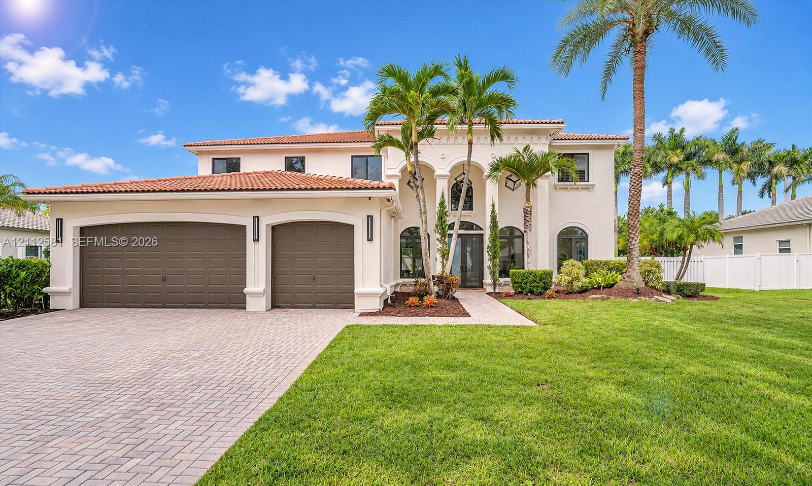 Stucco exterior featuring arched architectural detailing, a multi-car garage, clay tile roofing, a paved driveway, and established landscaping