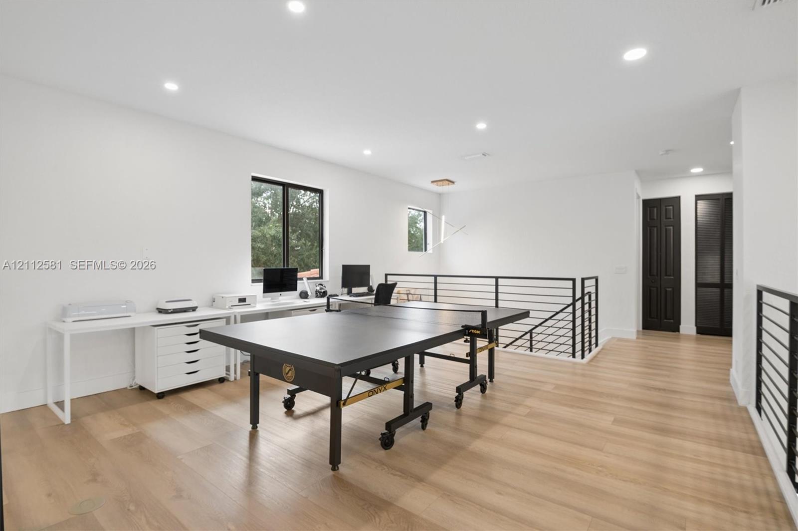 Open-concept room featuring light wood-finish flooring, recessed lighting, modern black metal railings, and dual interior doors with black finish