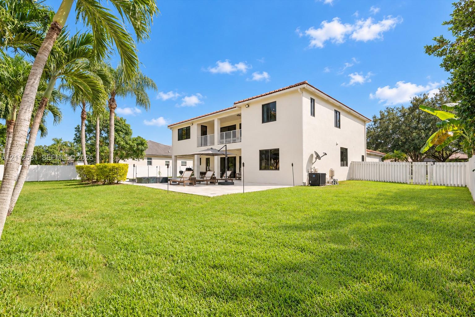 Two-story stucco exterior with a covered rear patio, balcony, fenced backyard, and manicured lawn