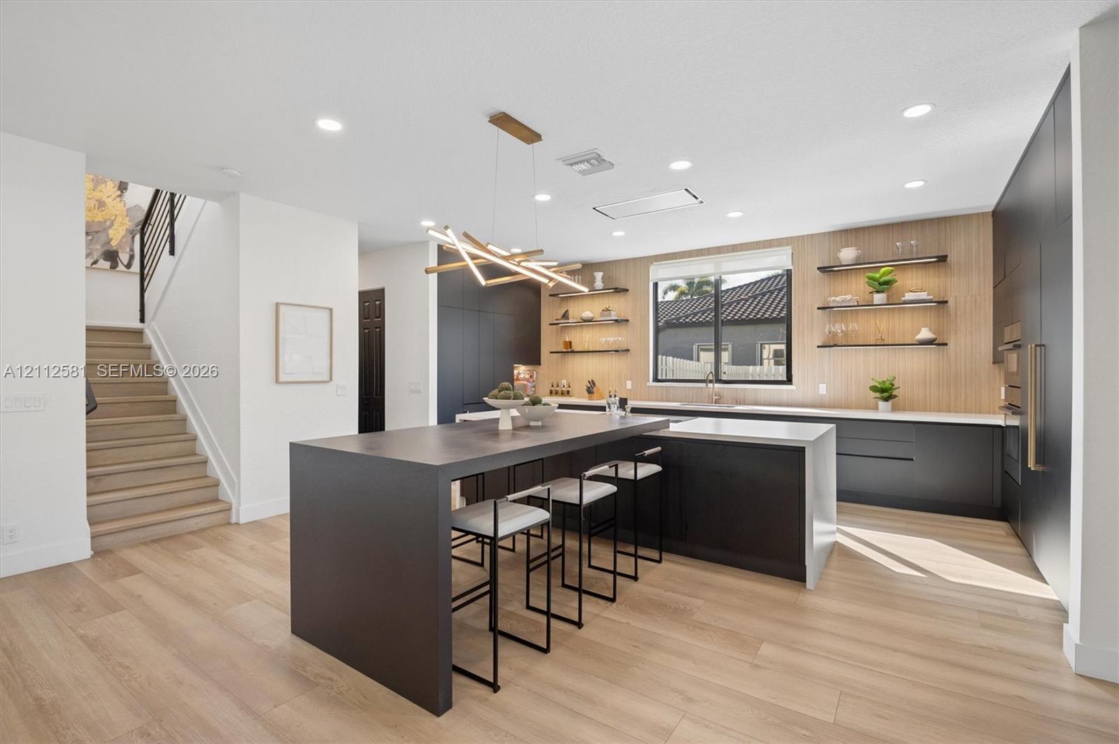 Modern kitchen featuring matte black cabinetry, waterfall-edge island, wood-finish flooring, floating shelving, and integrated recessed lighting