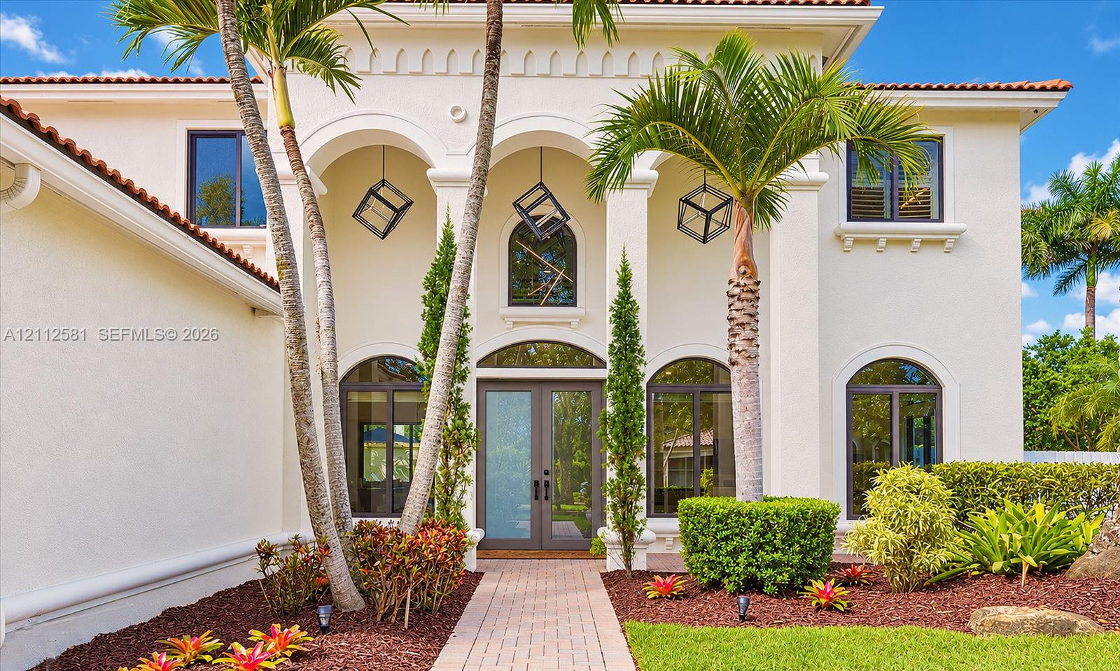 Mediterranean-style exterior featuring a covered entryway with structural arches, decorative pendant lighting, arched window accents, and a paved walkway