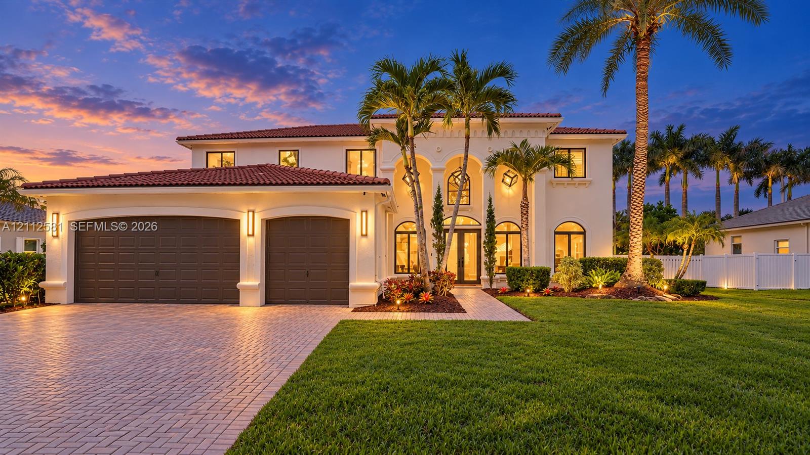 Mediterranean-style exterior featuring a clay tile roof, arched entryway, stucco facade, paved driveway, and integrated outdoor wall lighting