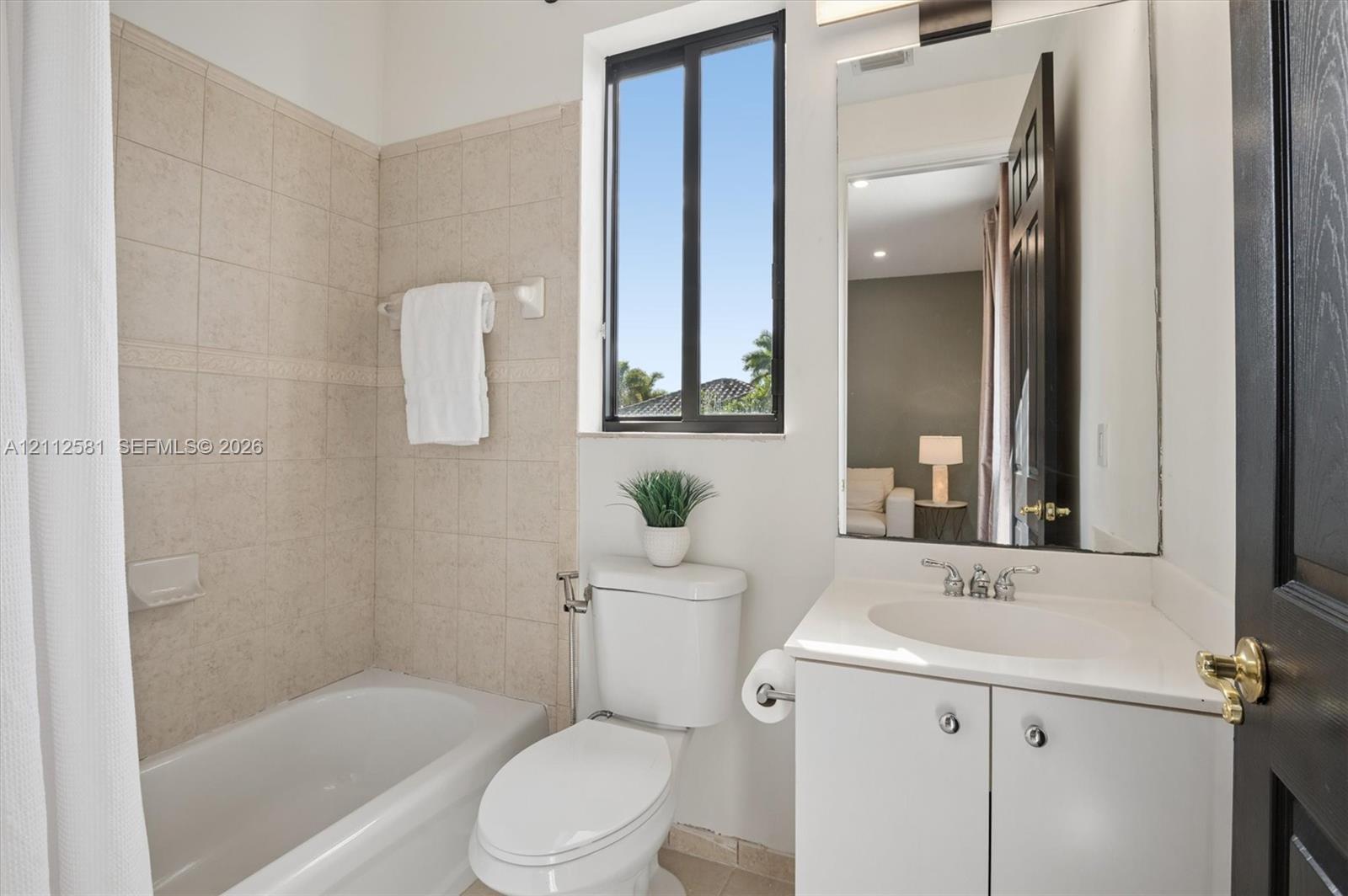 Bathroom featuring a white vanity with a composite countertop, an undermount sink with a polished chrome faucet, a wall-mounted mirror, and a tiled shower-tub combination