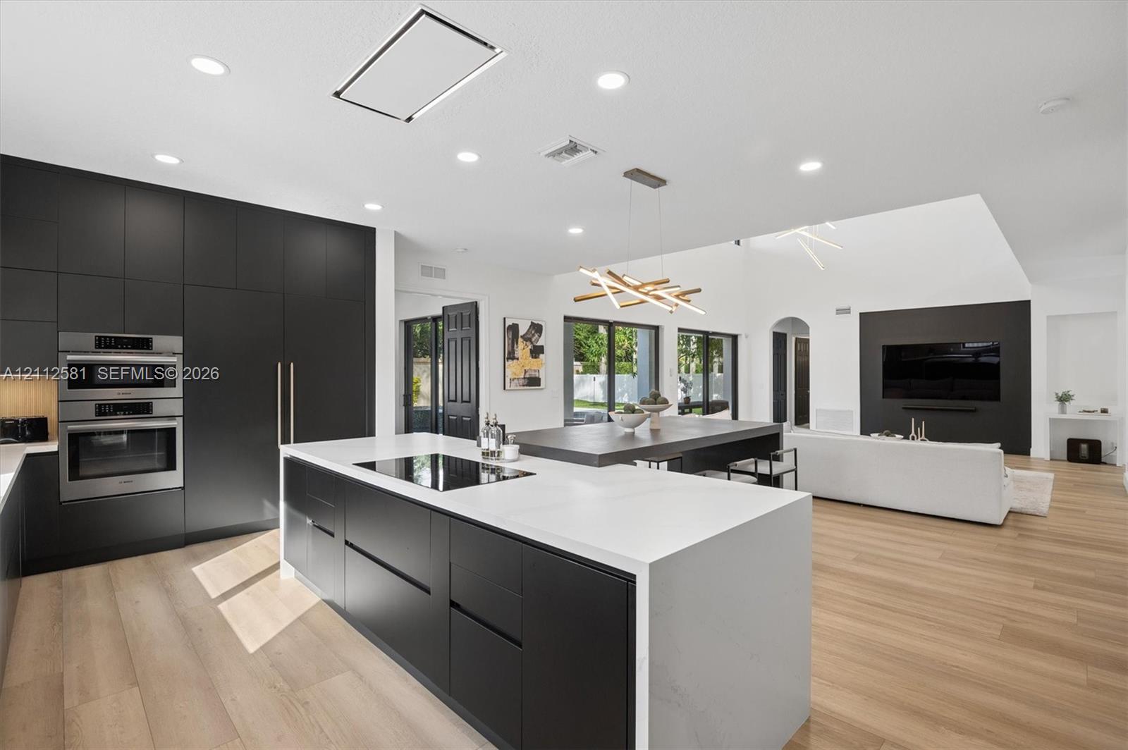 Kitchen featuring matte black floor-to-ceiling cabinetry, a central island with a waterfall-edge countertop, wood-finish flooring, recessed lighting, and stainless-steel built-in appliances