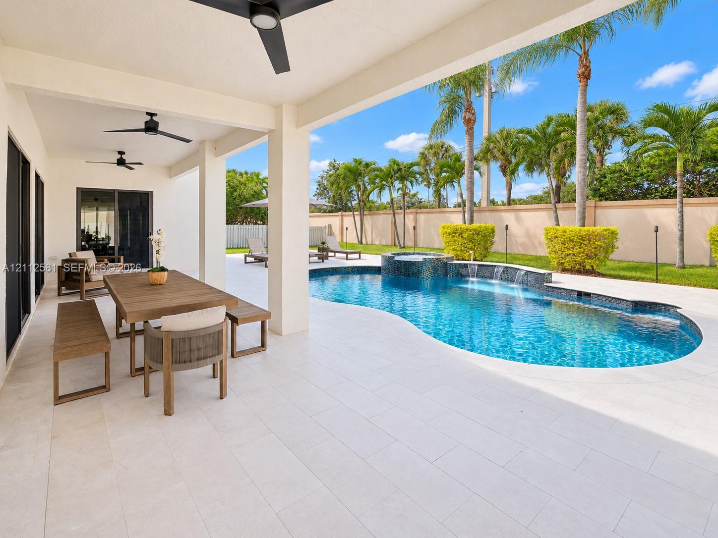 Covered outdoor patio featuring tile flooring, ceiling-mounted fans, a free-form pool with a raised spa, stone water features, and a privacy wall