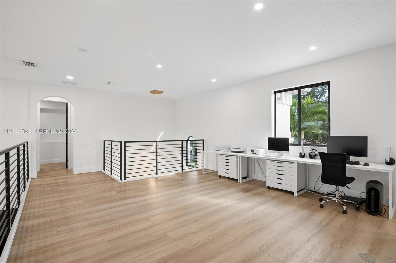 Open-concept area featuring wood-finish flooring, recessed lighting, and a black metal horizontal-bar railing