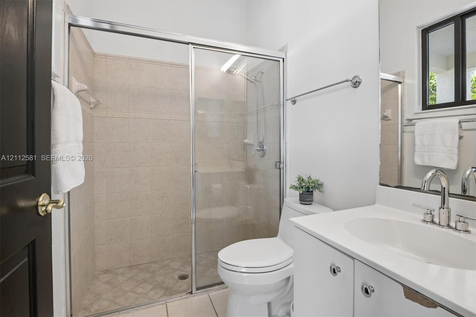 Walk-in shower with sliding glass door, tiled surround, and integrated shower head, paired with a white vanity featuring a rectangular undermount sink, chrome faucet, and expansive mirror